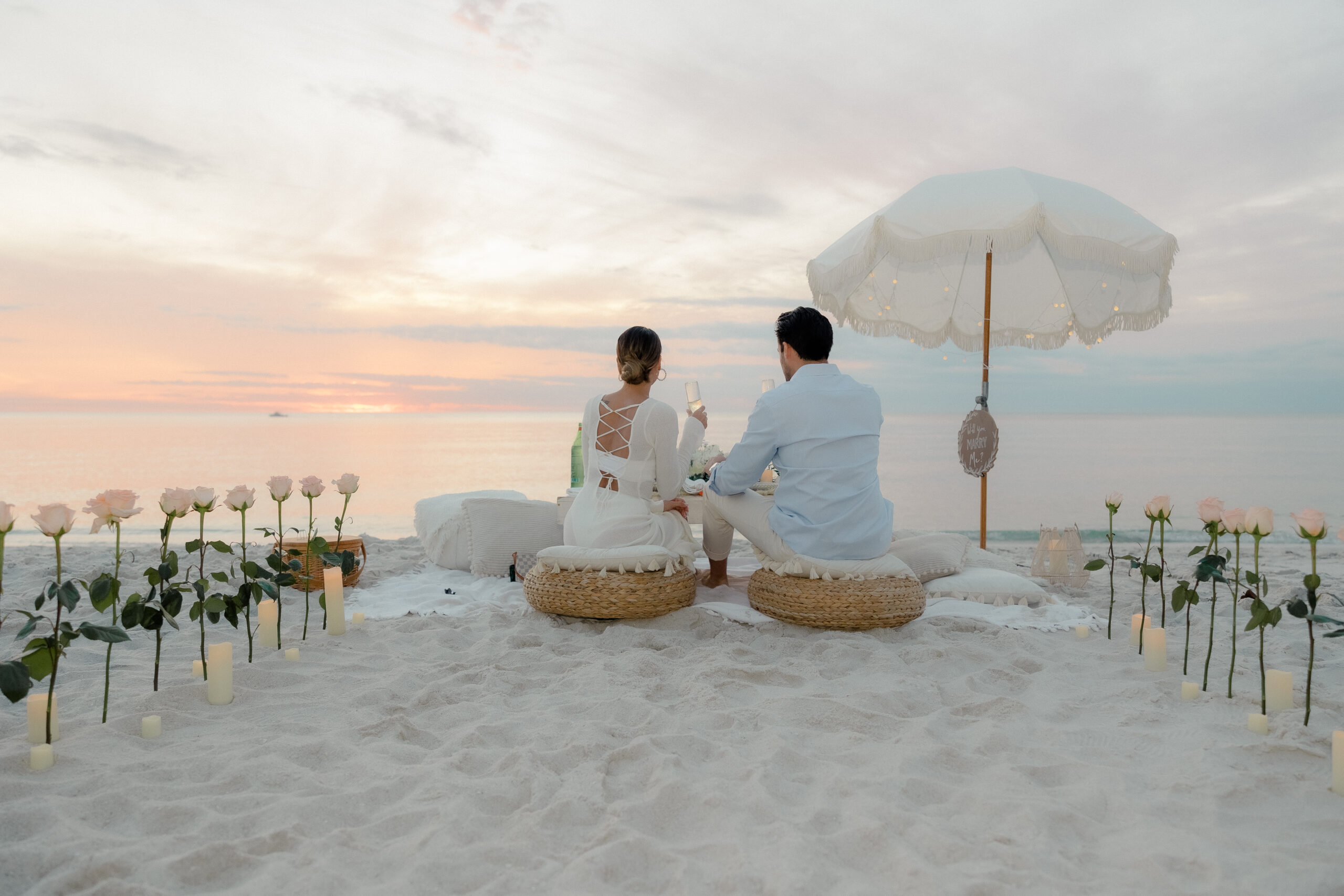 Engaged couple cheering at picnic beach setup for a proposal taken by a Naples Florida photographer.