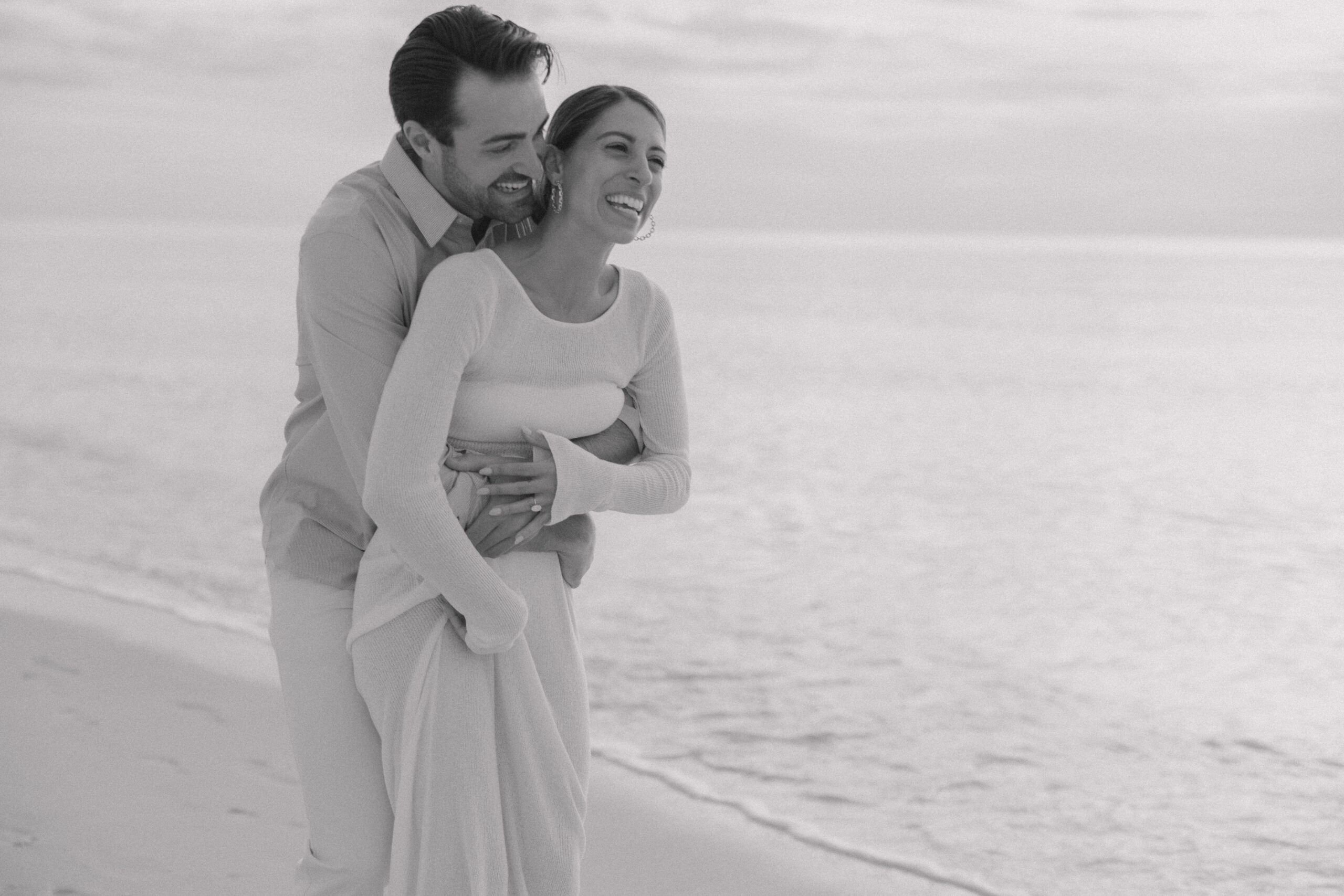 Candid shot taken by Naples photographer Maddie Briggs, freezing the genuine joy and radiant smiles of the newly engaged couple as they enjoy their post-proposal picnic on the Naples beach.